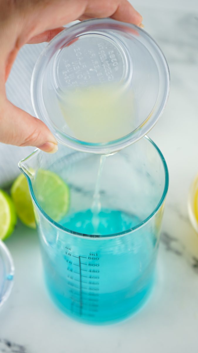 Pouring lime juice, blue curaçao and pineapple in pitcher