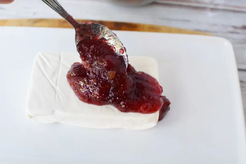 Pouring cranberry sauce over top of cream cheese