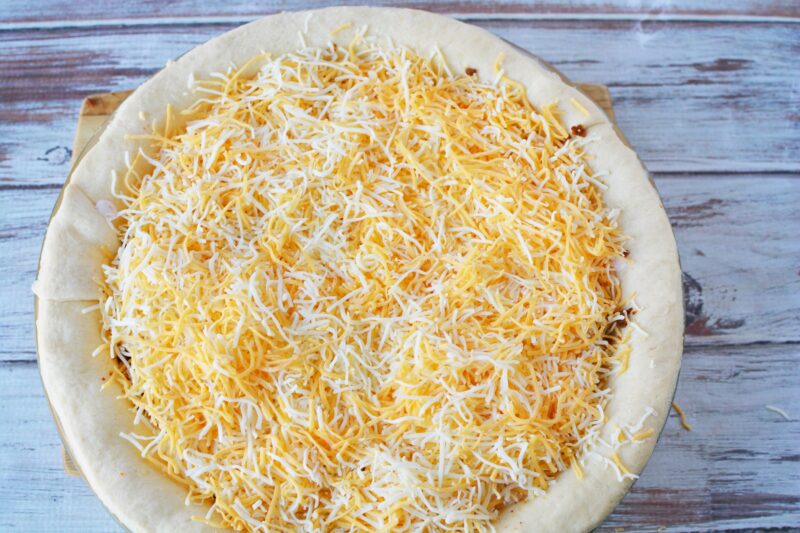 Adding shredded cheese on top of Doritos Taco Pie