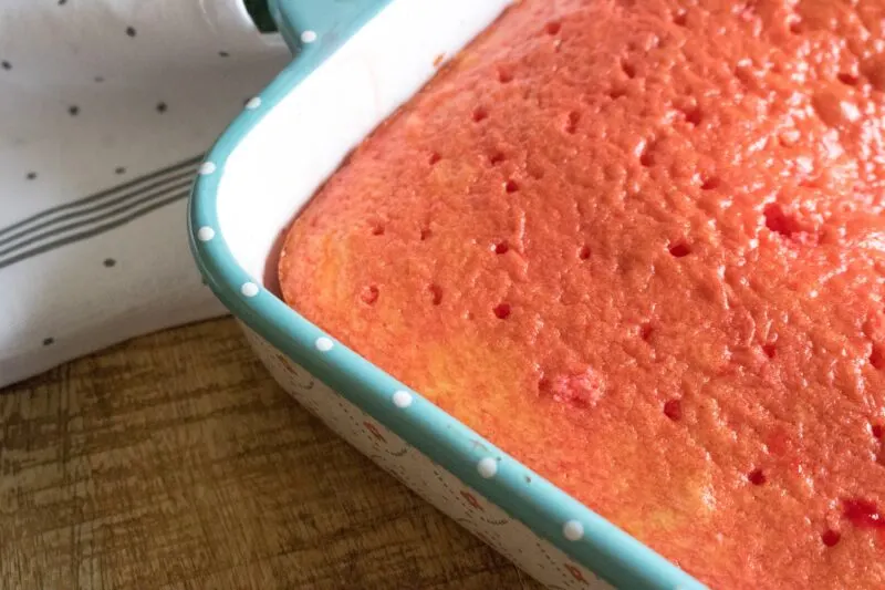 Pouring strawberry gelatin over the white cake mix