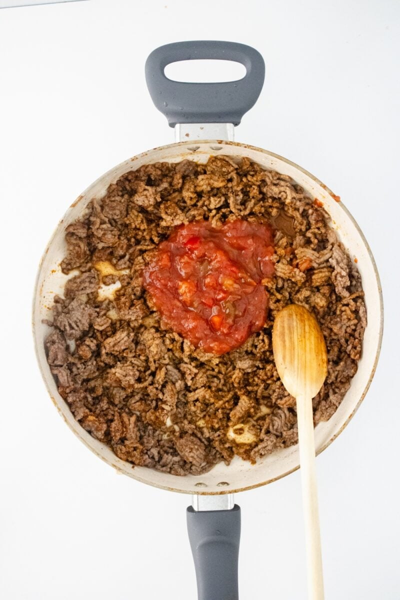 Adding salsa to ground beef mixture in stovetop pan.