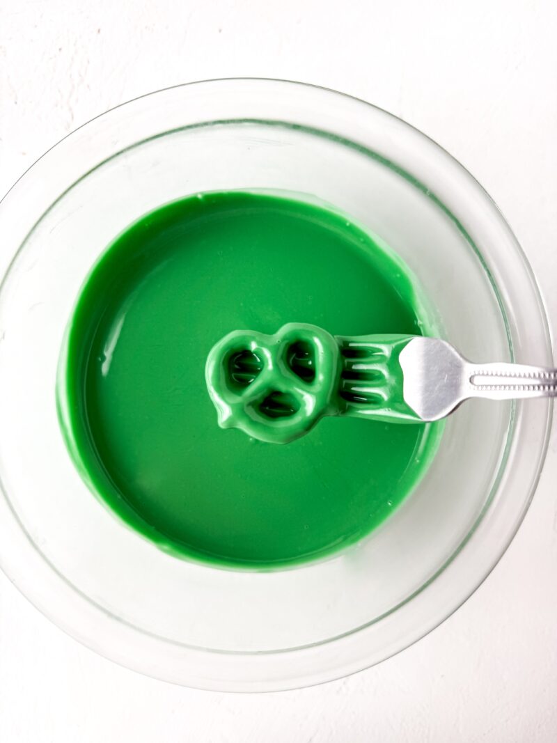 dipping pretzel twist into the green candy melt