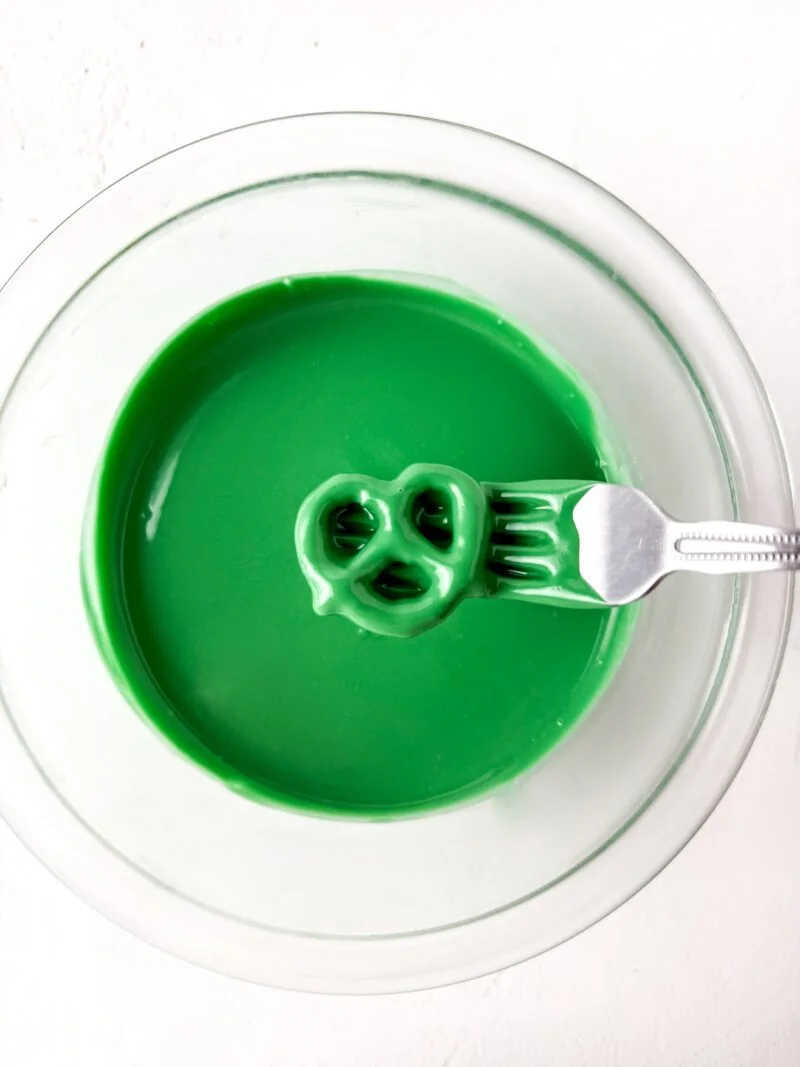 dipping pretzel twist into the green candy melt