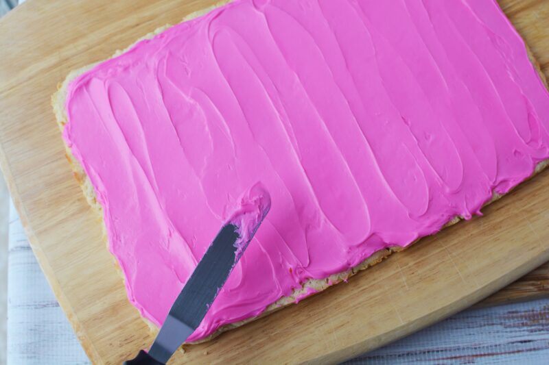 Spreading the pink frosting over the top of the cookie bars