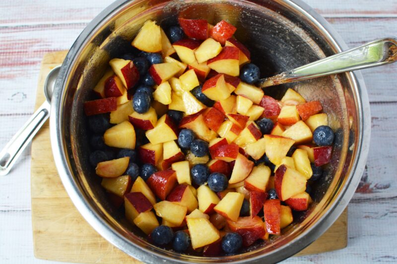 Mixing the peaches and the blueberries together in a mediaum bowl