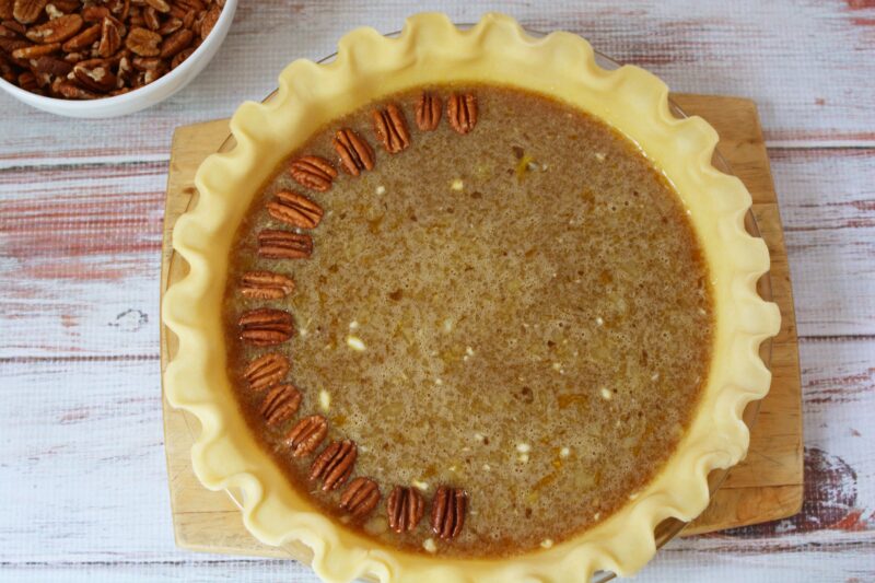 Pouring the pie batter into the pie crust and arranging the pecans on top.